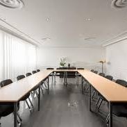 Salle de réunion moderne avec tables disposées en U et chaises noires.