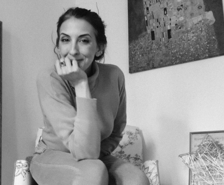 Femme souriante avec des cheveux roux, assise sur une marche en bois.