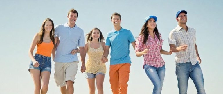 Groupe de jeunes adultes marchant sur la plage sous un ciel clair et ensoleillé.